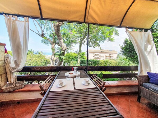An outdoor seating area with a table set for two, a view of greenery and a building in the background.