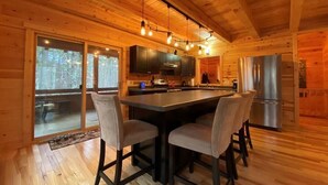 Interior de una cabaña de madera con una isla de cocina, taburetes de bar y un refrigerador grande.