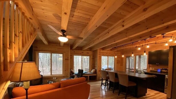 Interior de una cabaña de madera con sofá, mesa de comedor, sillas y zona de cocina.