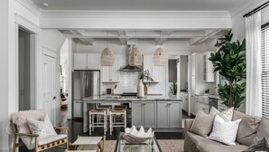 A modern kitchen with white cabinetry, a central island, and pendant lighting. There is a seating area with a sofa and chairs, and a large plant in the corner. - Salt In The City a Downtown Retreat-Hidden rooftop with Downtown Skyline Views. (Nashville)