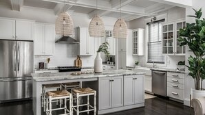 A modern kitchen with white cabinetry, a stainless steel refrigerator, a marble island, wicker pendant lights, and a large potted plant. - Salt In The City a Downtown Retreat-Hidden rooftop with Downtown Skyline Views. (Nashville)