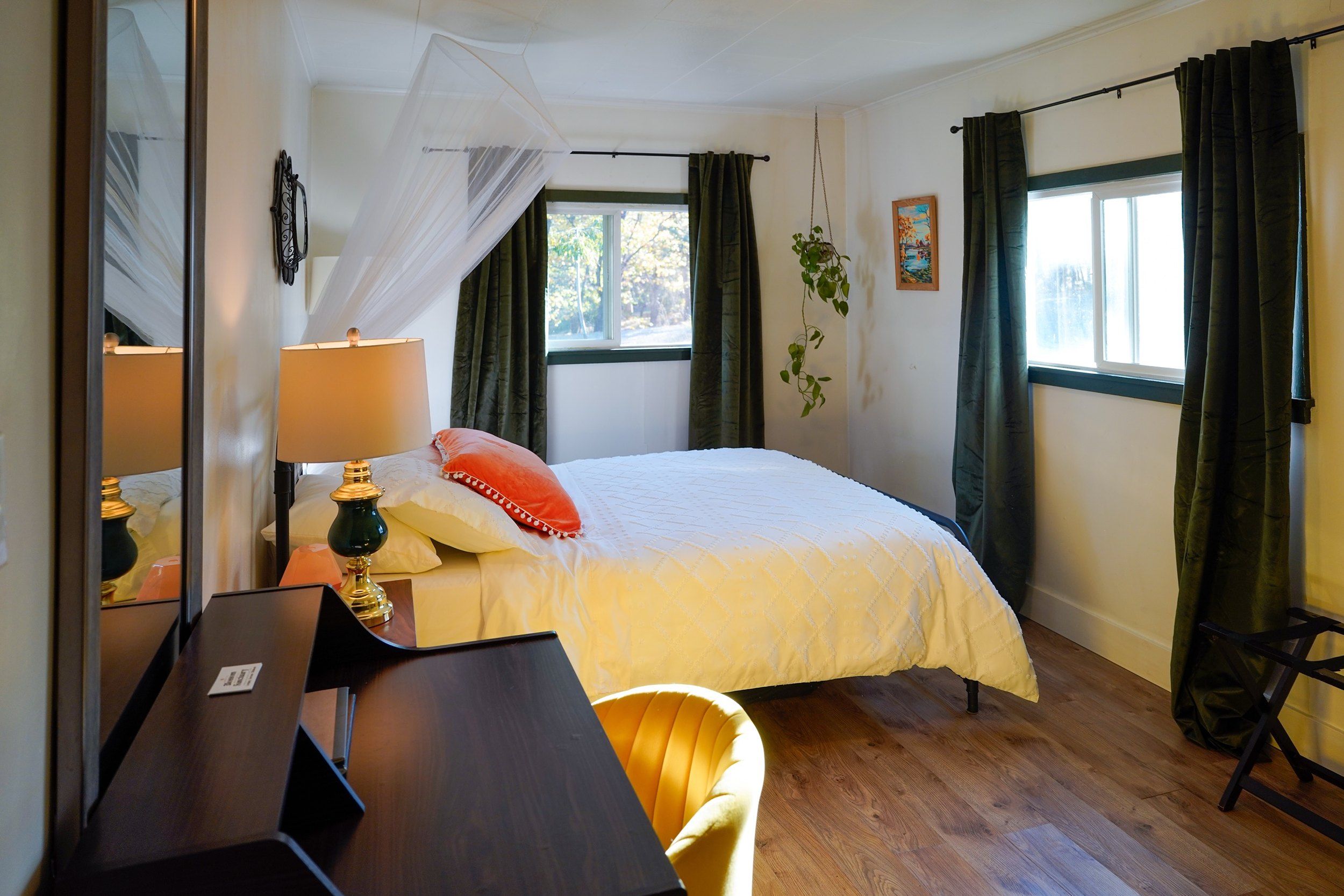 A hotel room with a bed, a desk, a chair, a window with curtains, and a bedside lamp.