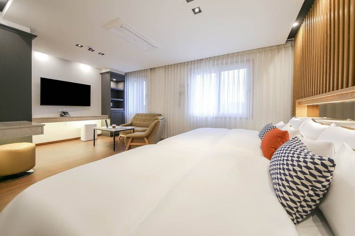 A modern hotel room with a large bed, a desk, a chair, and a TV mounted on the wall.