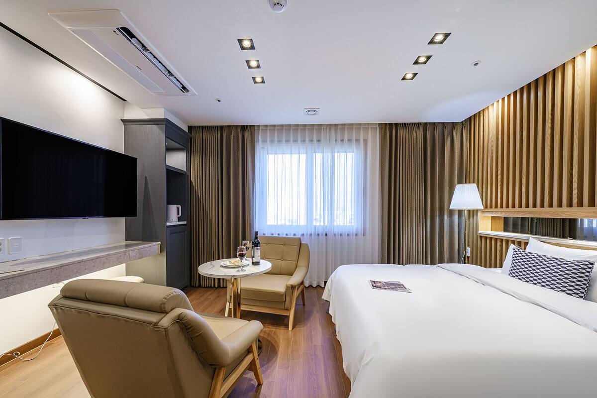 A hotel room with a bed, a desk, a chair, a TV, and a window with curtains.