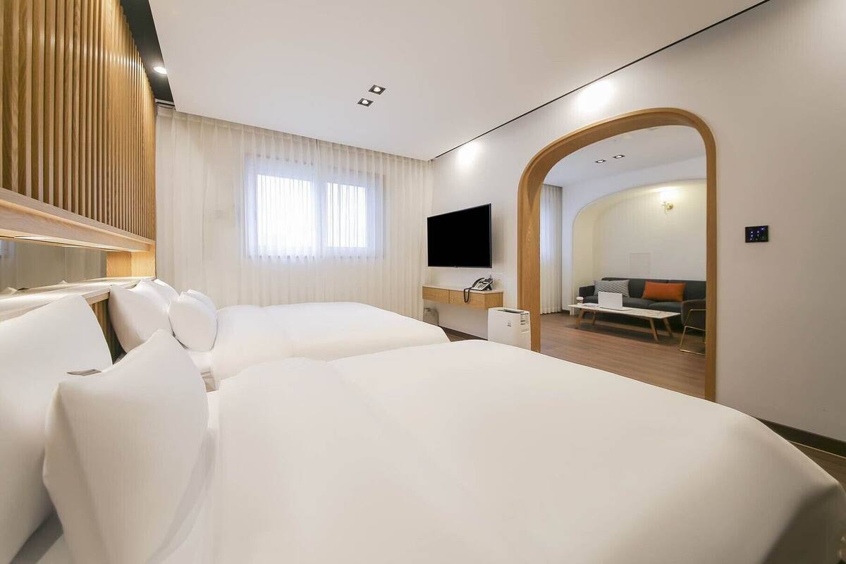 A hotel room with two beds, a TV, a desk, and a sofa in the adjacent living area.