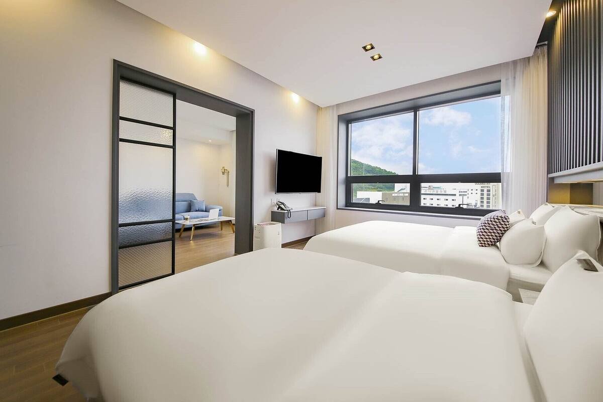 A hotel room with two beds, a TV, a desk, and a window with a city view.
