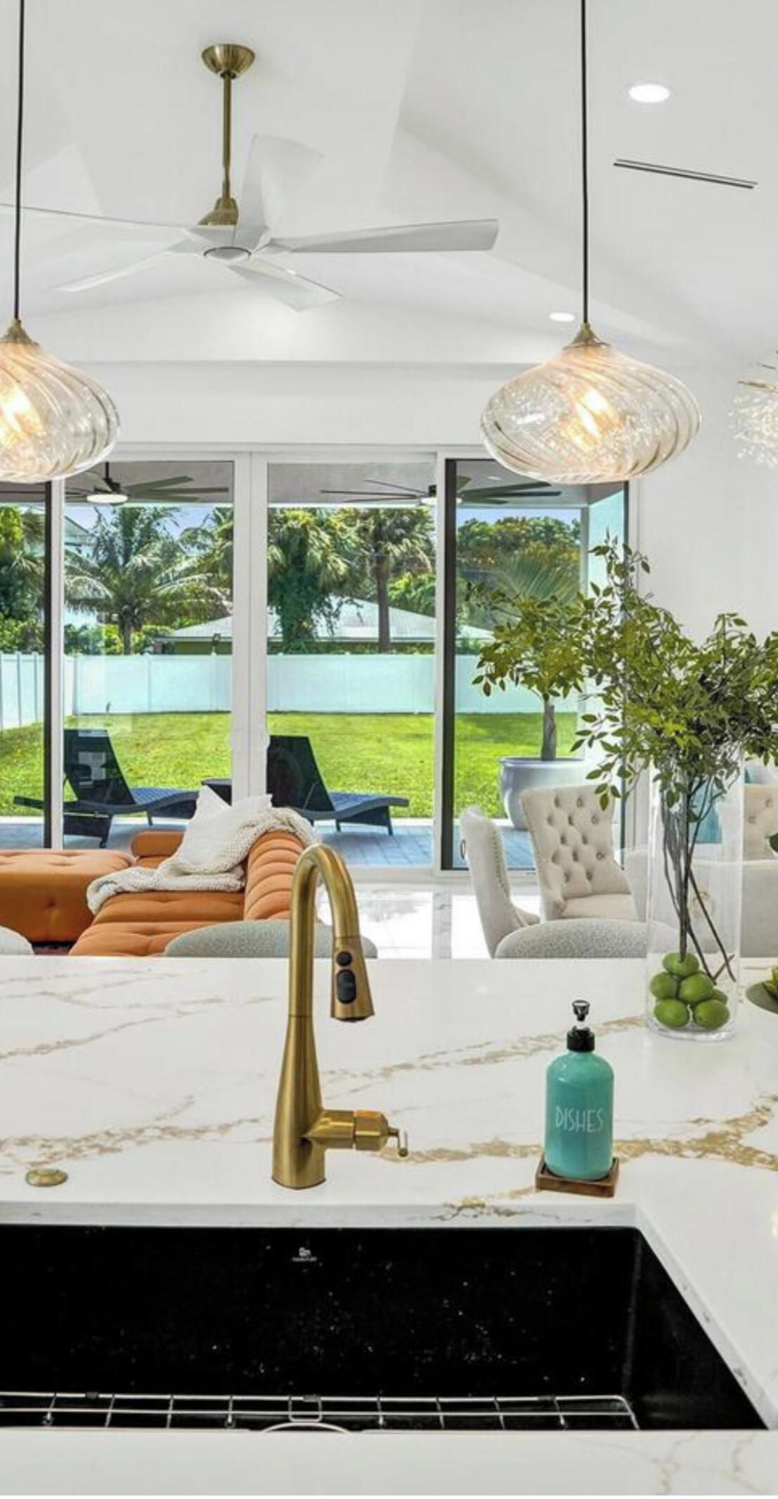 A modern kitchen with a marble countertop, a gold faucet, and a view of the outdoors.