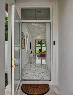 A modern interior with a glass door leading to a living area, a marble floor, and a chandelier.