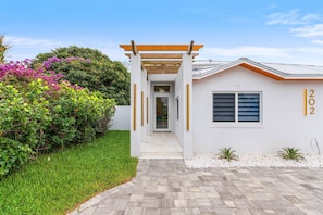 A modern house with a white exterior, a wooden pergola entrance, and a number '202' on the wall.