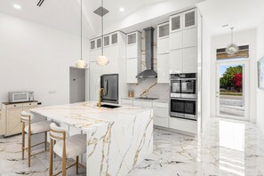 A modern kitchen with white cabinetry, a marble island, stainless steel appliances, and pendant lighting.
