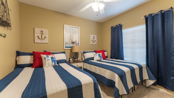 A bedroom with two beds, nautical-themed decor, a ceiling fan, and a window with curtains.