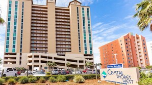 Un hotel de varios pisos con una estructura de estacionamiento central, un letrero que indica '931 West Beach Blvd' y el logotipo de 'Crystal Shores West'.