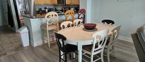 Una cocina con armarios de madera, un refrigerador, un microondas y una zona de comedor con una mesa y sillas.