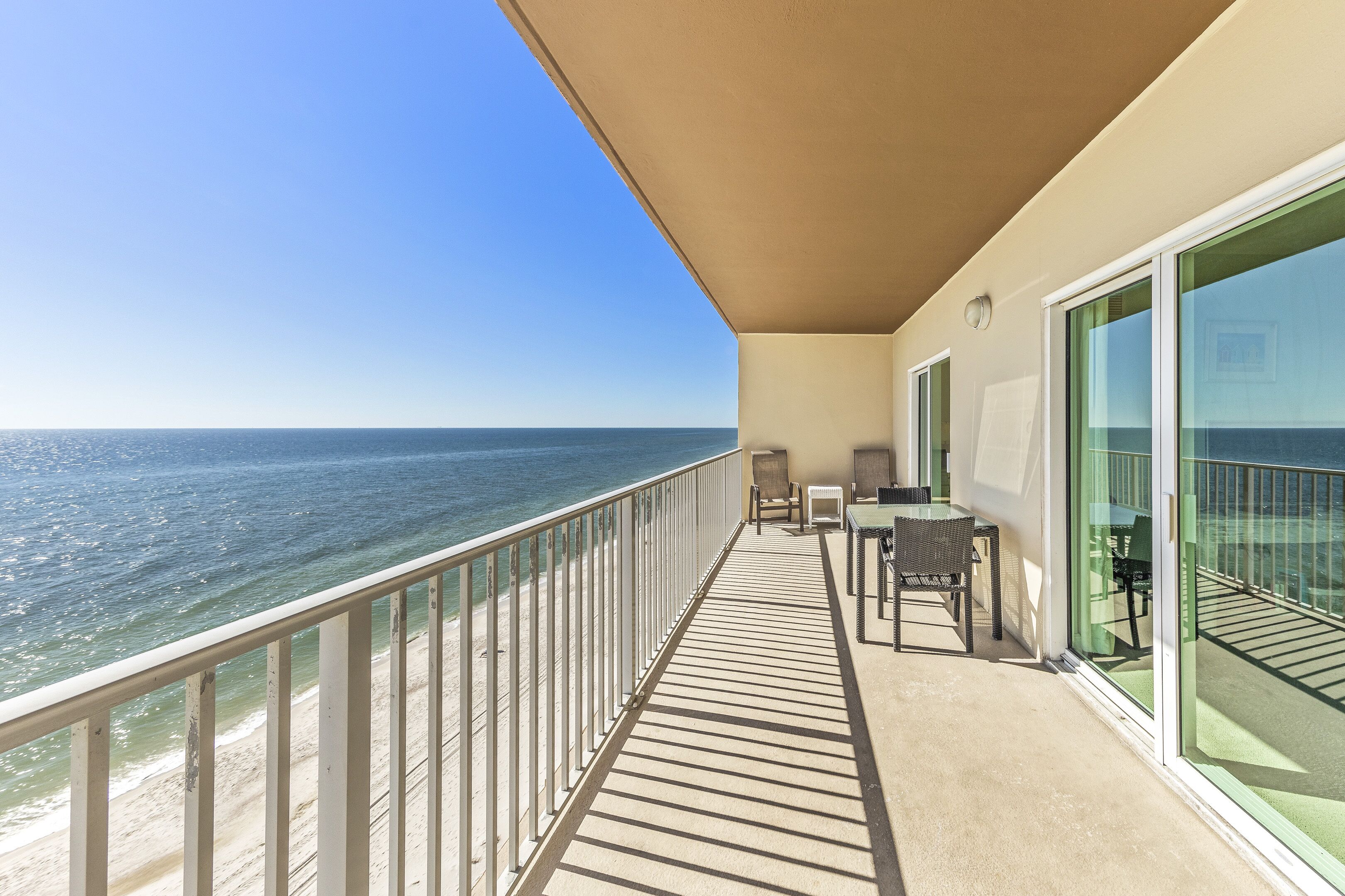 A balcony with a view of the ocean, a table, chairs, and a glass door.