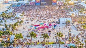 Una playa concurrida con un escenario y carpas, rodeada de edificios altos.