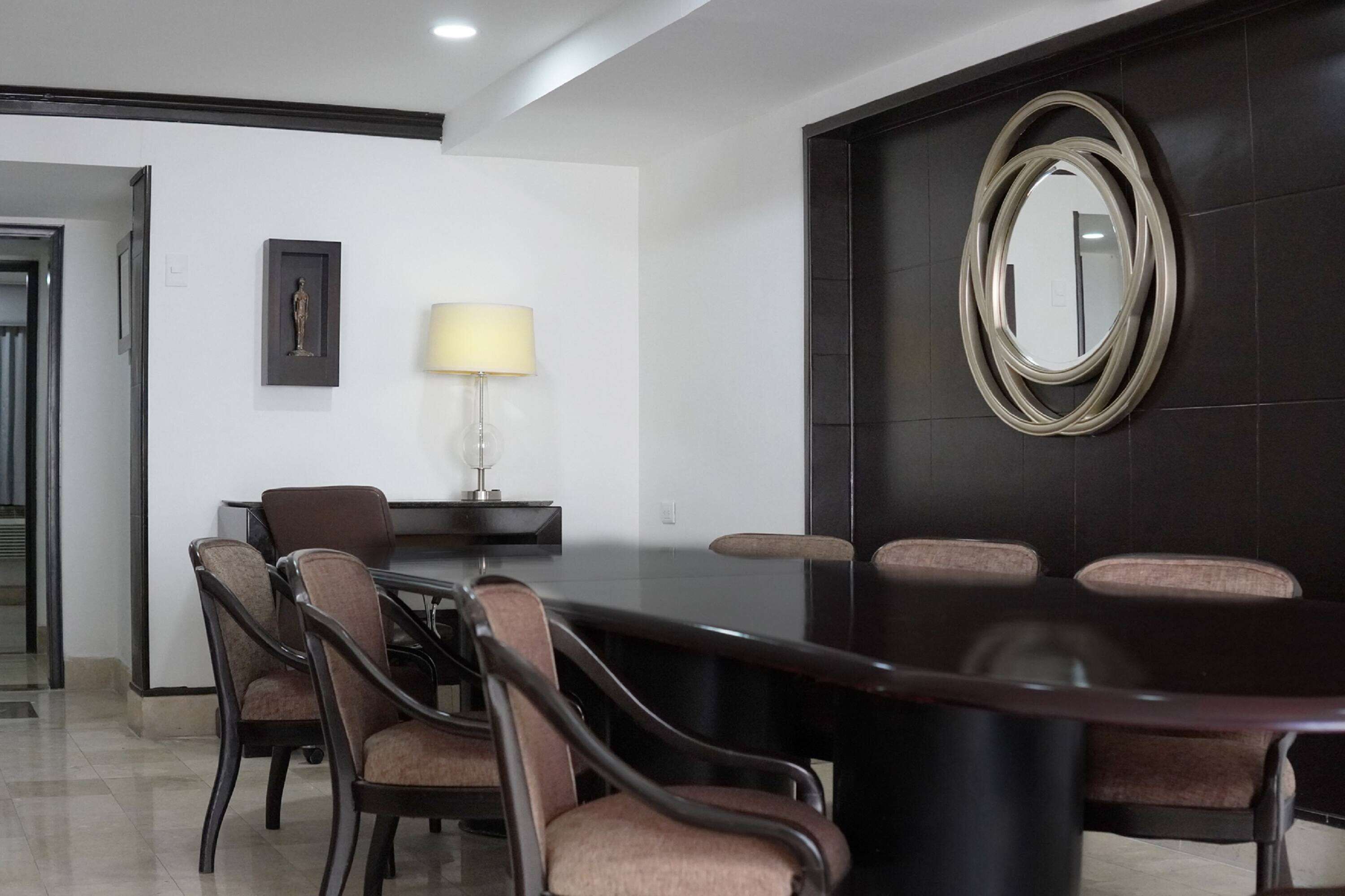 Un salón de conferencias con una mesa de madera oscura, seis sillas, una lámpara y un cuadro en la pared.