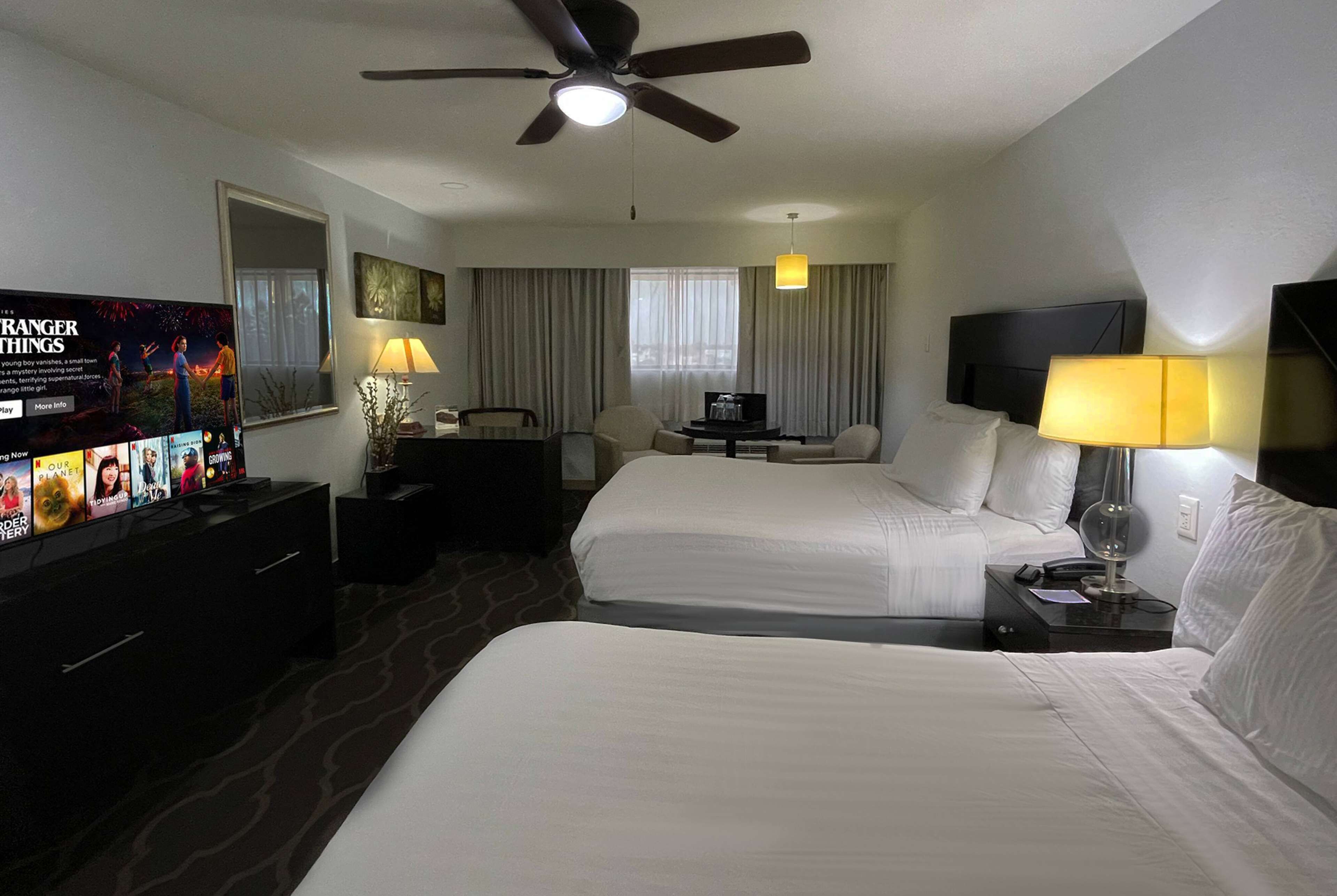A hotel room with two beds, a TV, a ceiling fan, and a desk with a lamp.