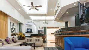 A spacious lobby with a high ceiling, a ceiling fan, a reception desk, a blue armchair, and a sofa with cushions. - Wyndham Garden Los Mochis Plaza Inn (Los Mochis)
