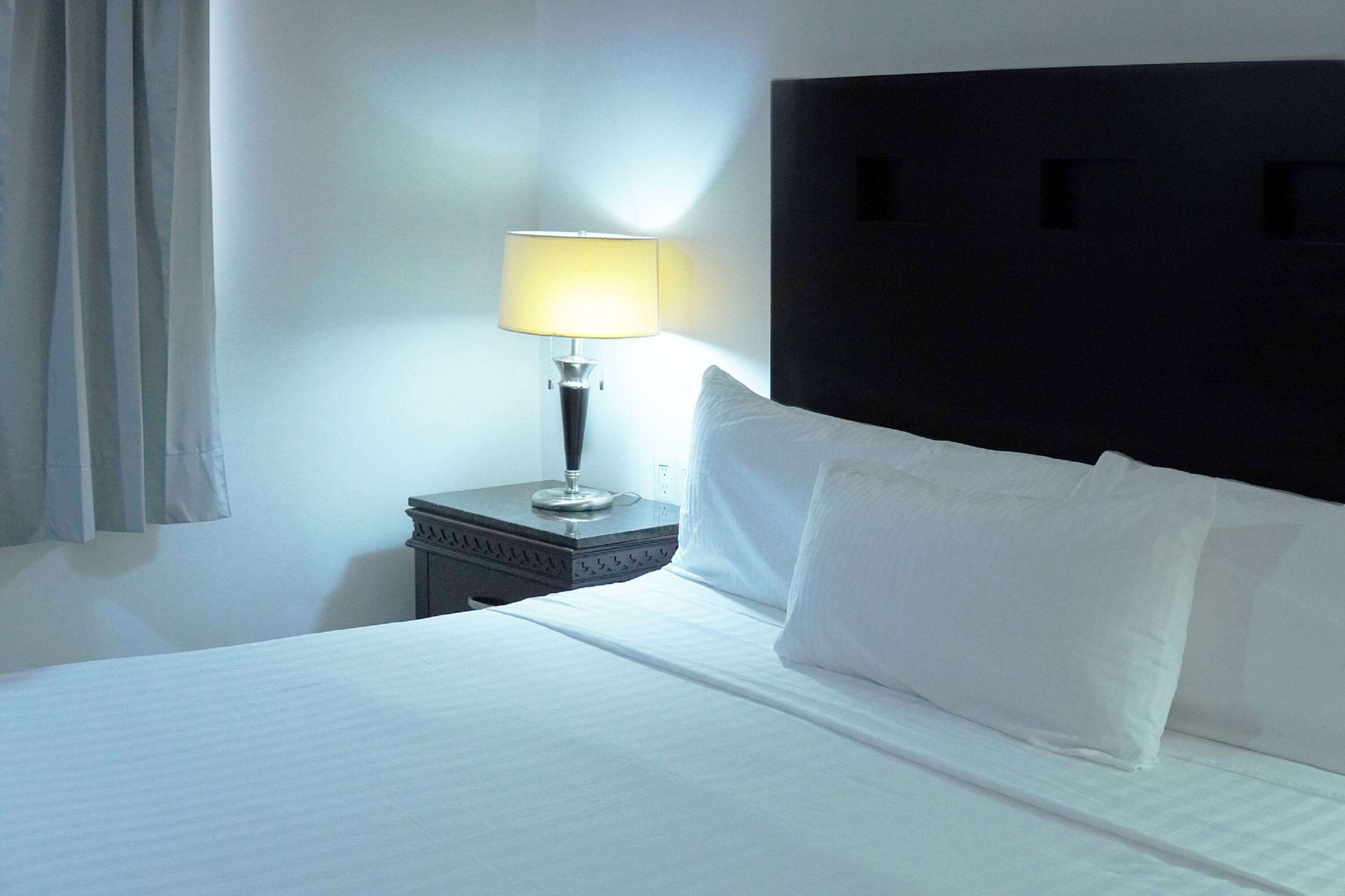A neatly made bed with white linens and pillows, a bedside lamp, and a dark headboard.
