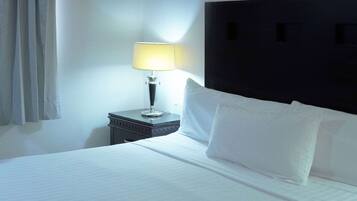 A neatly made bed with white linens and pillows, a bedside lamp, and a dark headboard.