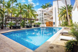 A swimming pool with lounge chairs and a covered seating area, surrounded by palm trees and a multi-story building. - Wyndham Garden Los Mochis Plaza Inn (Los Mochis)