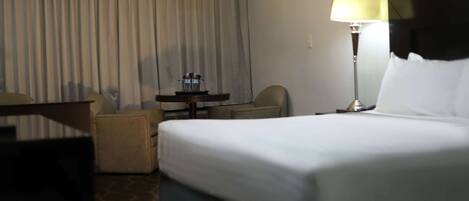 Una habitación de hotel con cama, escritorio, silla, lámpara y cortina.