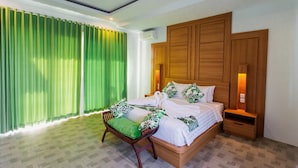 Een netjes ingerichte slaapkamer met een bed, een houten nachtkastje, een bankje met kussen en een groot raam met groene gordijnen.