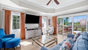Ein geräumiges Wohnzimmer mit einem großen Glastisch, einem blauen Sofa und einem Deckenventilator.