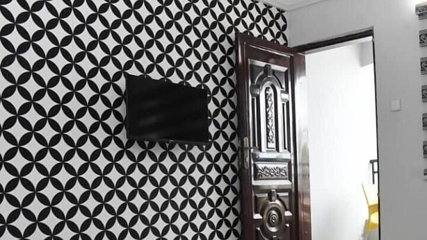 Una habitación con pared de diseño geométrico, un armario negro y una puerta de detalles ornamentales.