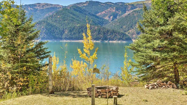 A lakeside view with a wooden bench, a pile of logs, and a flag. - Irwin A-Frame Cabin w/ Deck & Mountain Views! (Irwin)