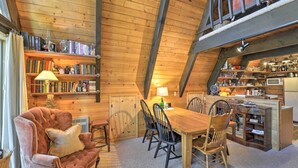 A cozy, rustic interior with a wooden ceiling, a dining area with a wooden table and chairs, a bookshelf filled with books, and a kitchen area with a microwave and various kitchen items. - Irwin A-Frame Cabin w/ Deck & Mountain Views! (Irwin)