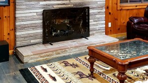 A rustic cabin interior with a stone fireplace, wooden walls, a leather couch, and a patterned rug.