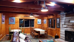 A cozy cabin interior with wooden walls, a dining area, a fireplace, and framed pictures on the walls.