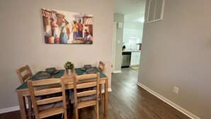 Uma área de refeições com mesa e cadeiras de madeira, toalha de mesa verde e uma pintura sobre a mesa.