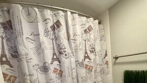 Casa de banho com cortina de chuveiro com motivos parisienses, sanita e toalheiro com uma toalha verde.