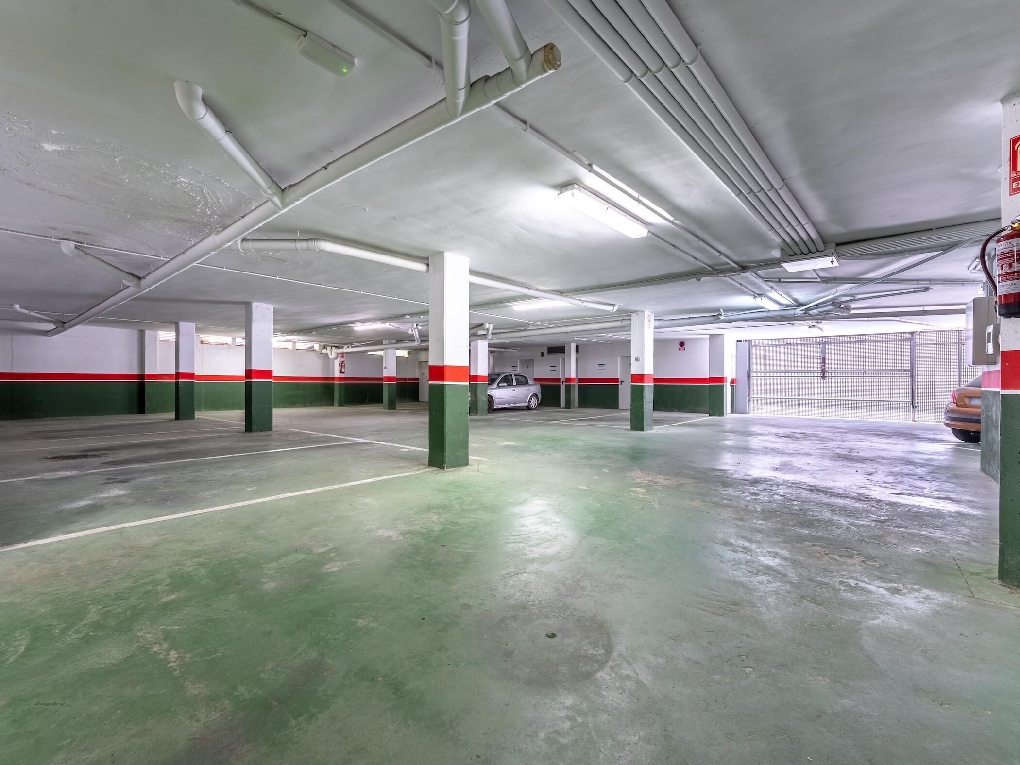 Un parking intérieur doté de nombreuses places de stationnement, de sols en béton et de murs peints en vert et en rouge.