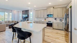 A modern kitchen with a central island, built-in appliances, and a dining area with black chairs. - Rock 'n' Roll Villa with Splash Pad at Encore (Kissimmee)