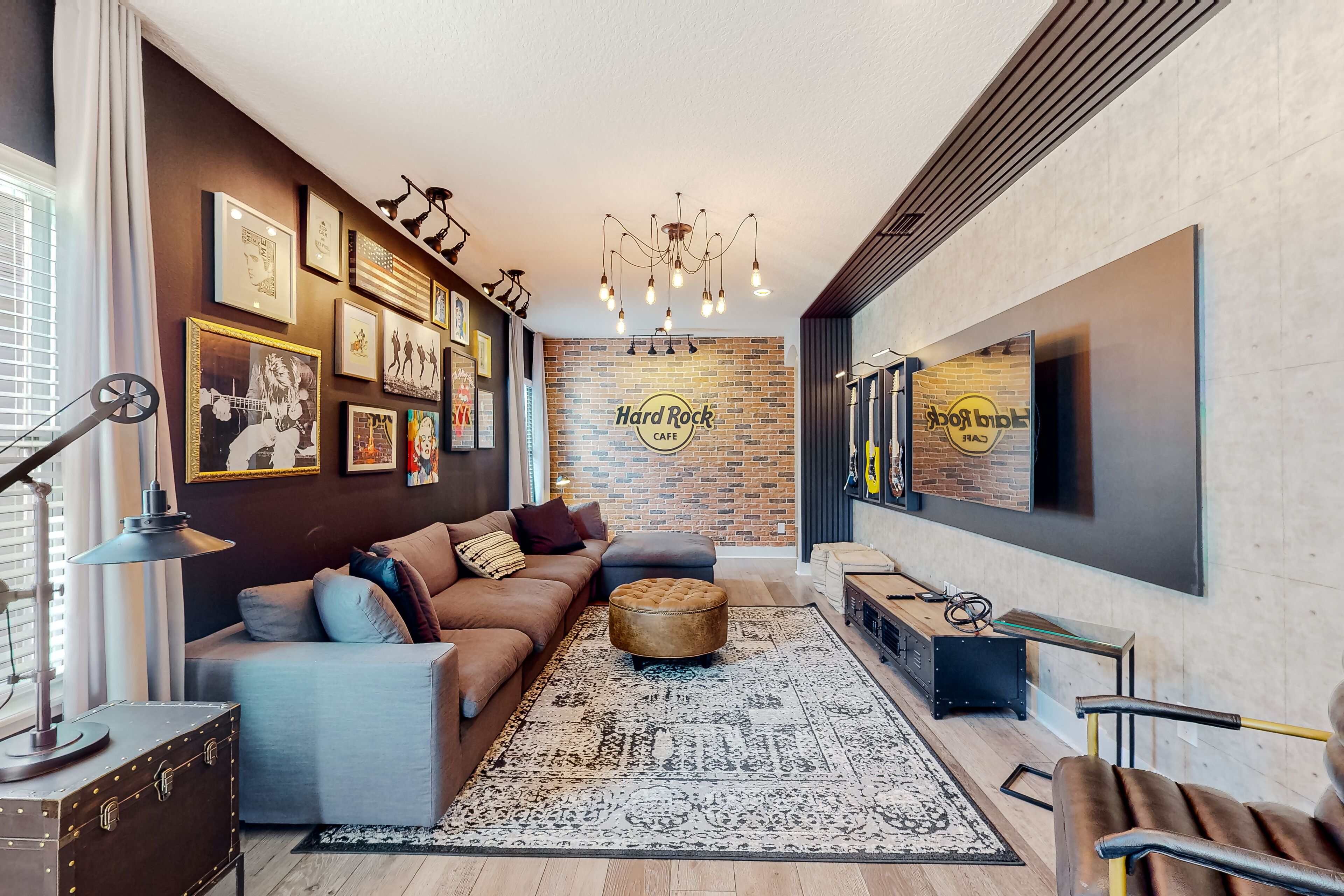 Una sala de estar moderna con un sofá marrón, un otoman redonda, una alfombra estampada y una pared de ladrillo con un letrero de 'Hard Rock Cafe'.