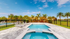 A rectangular swimming pool with a fountain, surrounded by a black fence, and a clear blue sky above. - Rock 'n' Roll Villa with Splash Pad at Encore (Kissimmee)