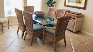 A dining area with a glass-top table surrounded by wicker chairs with green cushions. - It's a Fantasea-78 TP (Laguna Vista)