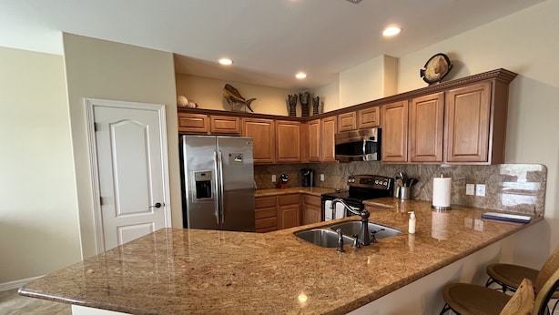 A kitchen with granite countertops, stainless steel appliances, wooden cabinets, and a built-in island with bar stools. - It's a Fantasea-78 TP (Laguna Vista)