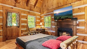 A log cabin bedroom with a bed, a fireplace, and a TV mounted on the wall.
