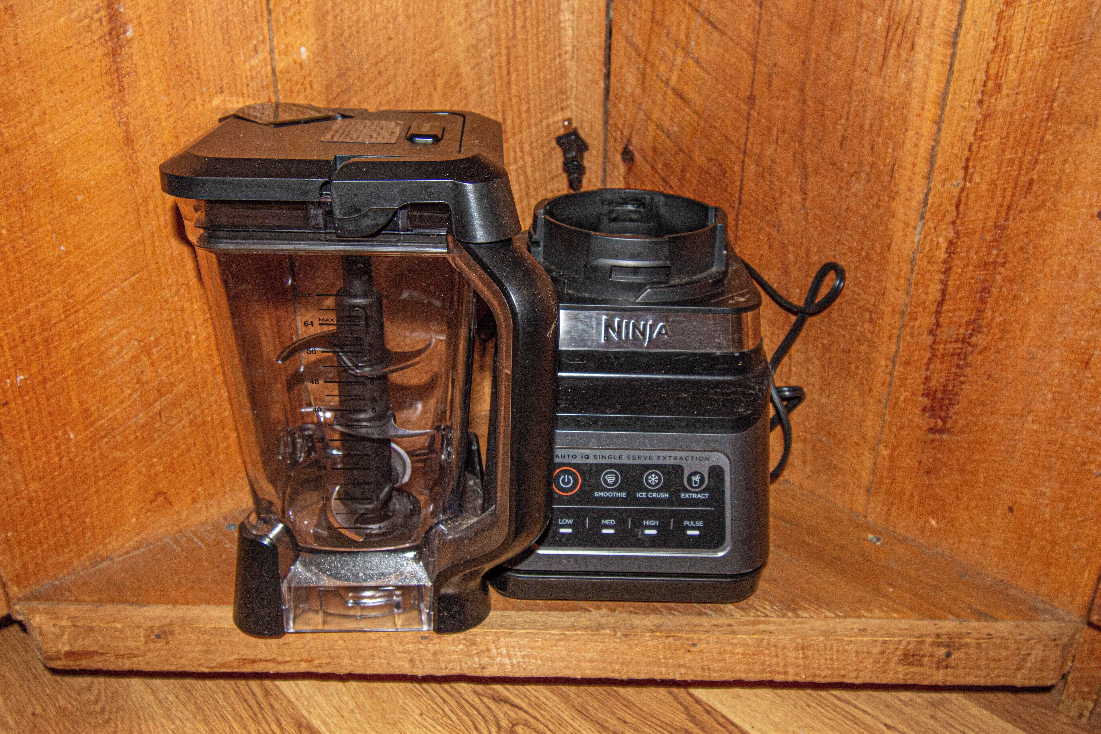A Ninja blender and a glass container on a wooden shelf.