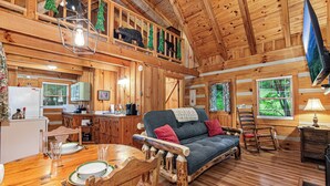 A cozy cabin interior with a wooden dining table, a sofa, and a television.