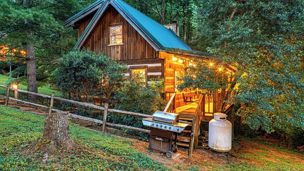 A rustic cabin with a metal roof, a wooden deck, and a barbecue grill.