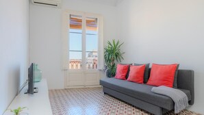 Un salon moderne avec un canapé gris, des coussins rouges, une petite plante et un sol carrelé.