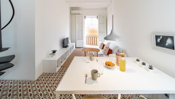 Une cuisine moderne avec une table blanche, un luminaire suspendu et une vue sur l’espace repas.