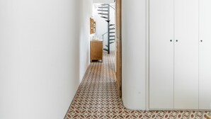 Un couloir étroit avec des carreaux de sol à motifs, une armoire en bois et une porte blanche.