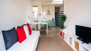 Un salon moderne avec un canapé, un téléviseur et une cuisine en arrière-plan.