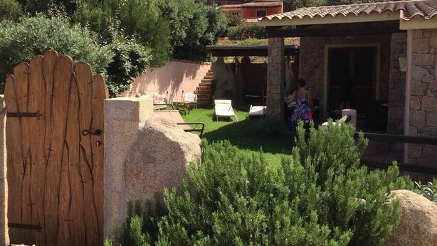 Un bâtiment en pierre avec un toit en tuiles, une porte en bois et un espace herbeux aménagé avec des chaises.